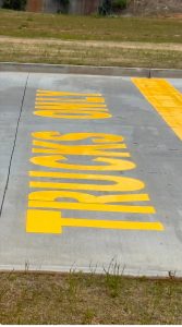 Large yellow letters painted along a concrete roadway edge beside a grassy verge.